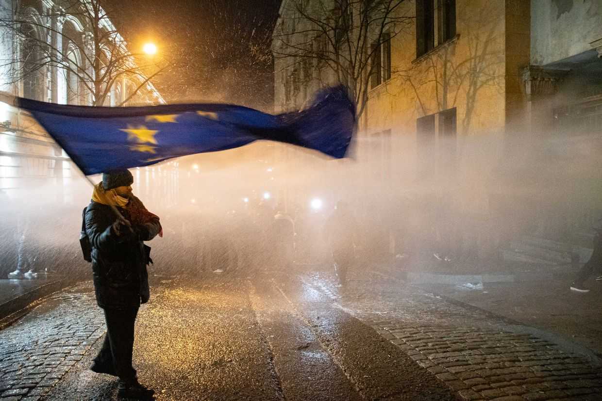 A protester waves an EU flag on a side street along the parliament building as water cannons are aimed at demonstrators on 28–29 November 2024. Photo: Mariam Nikuradze/OC Media.