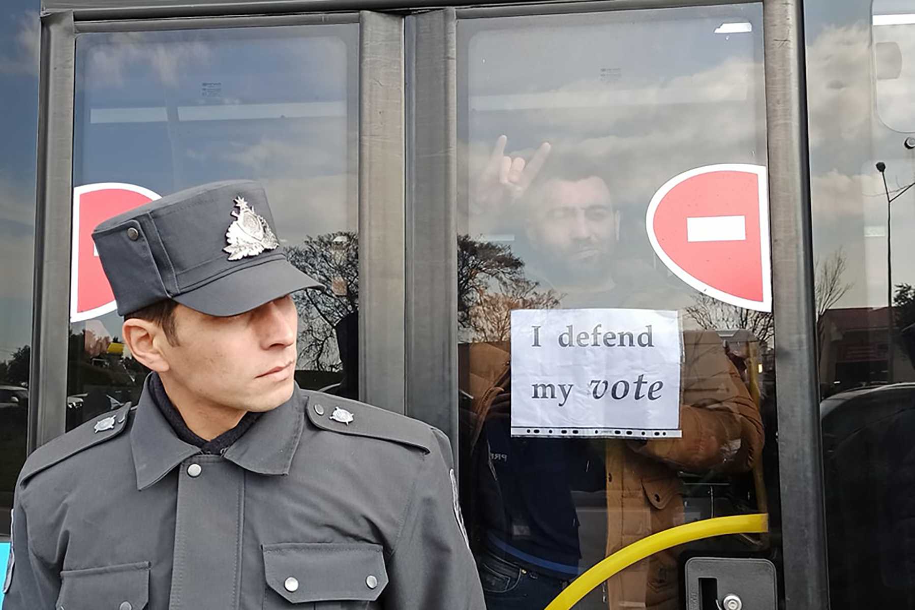 A police officer stands near a bus with protesters inside. Photo: Nurlan Gakhramanli