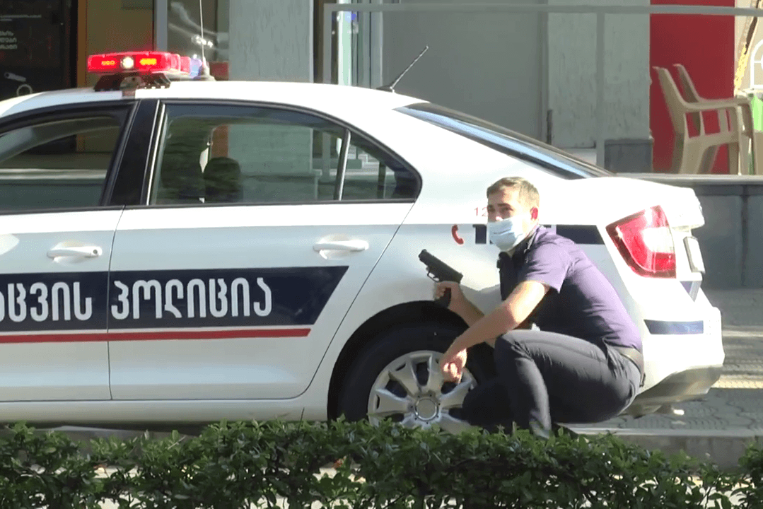 A police officer takes cover near the scene of the hostage crisis. Image via Odishi TV.