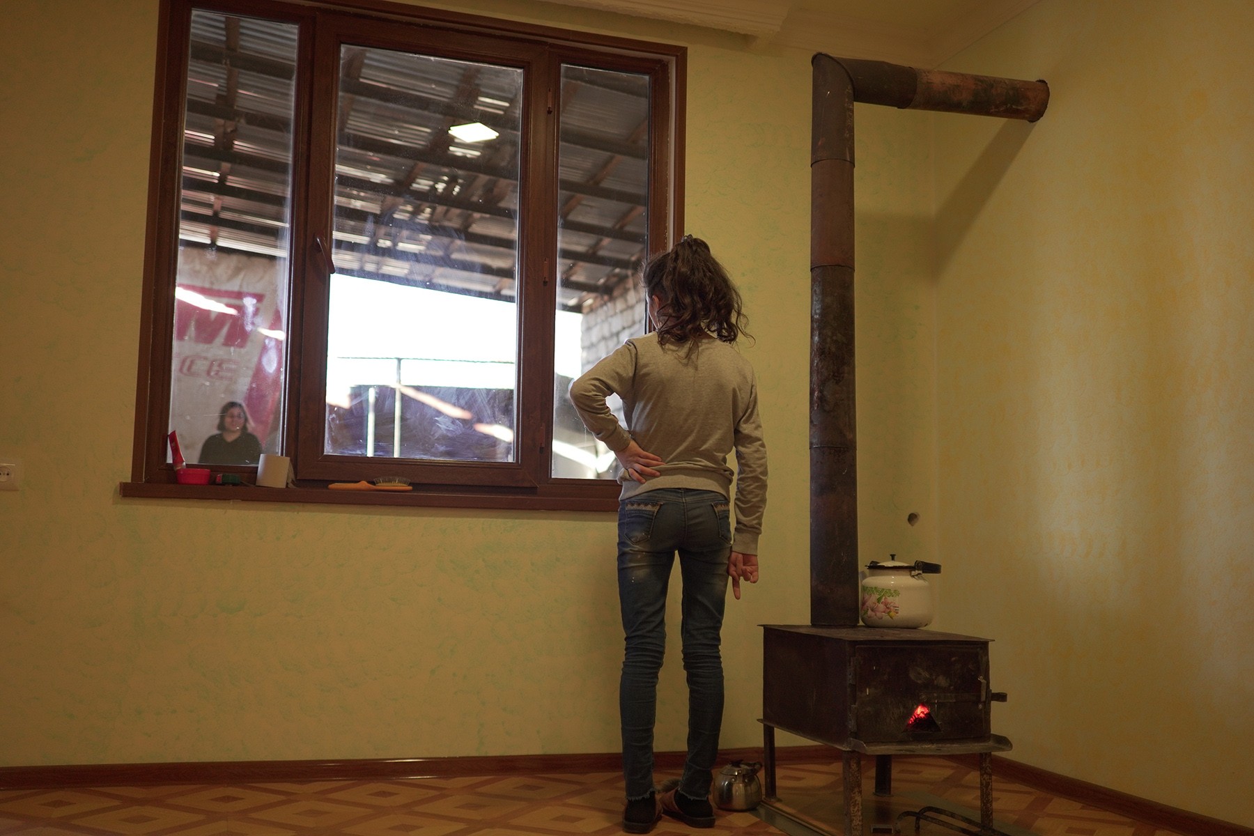A young girl stands by a wood-fired heater in the village of Mkhitarashen (Mukhtar).