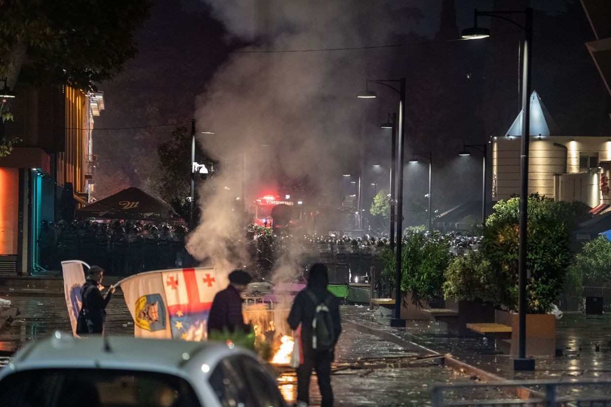 Protesters stand in front of a lit barricade on 4 October as riot police gather in the background. Photo: Mariam Nikuradze/OC Media.