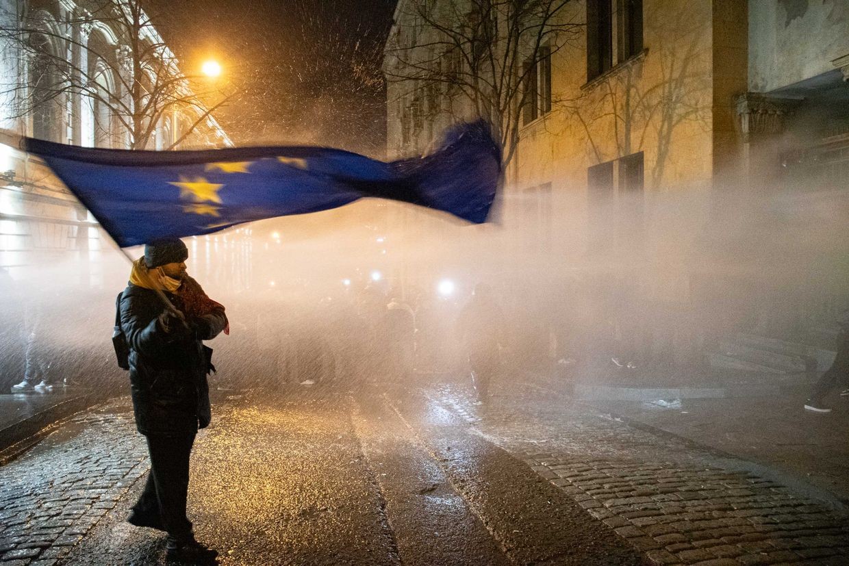 A protester waves an EU flag on a side street along the parliament building as water cannons are aimed at demonstrators on 28–29 November 2024. Photo: Mariam Nikuradze/OC Media.