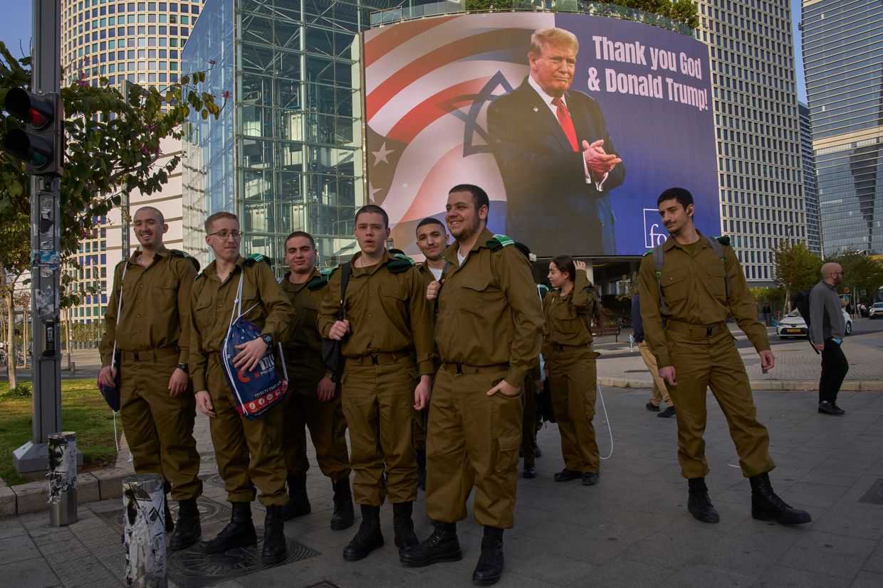 Israeli soldiers in Tel Aviv pass by an electronic billboard displaying an image of US President Donald Trump alongside the message 'Thank you God and Donald Trump', referring to the US involvement in the war between Israel and Iran in March 2026. Photo: AP Photo/Ohad Zwigenberg.