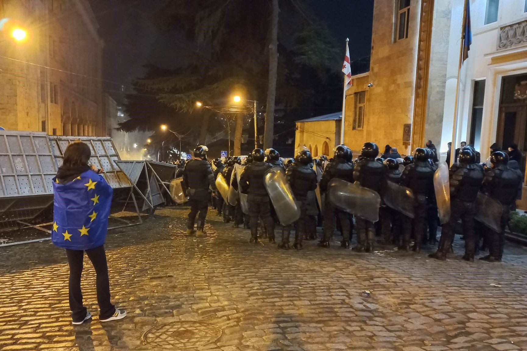 A woman draped in an EU flag watches on as riot police move in on protesters on 9 March. Photo: Anna Edgar/OC Media.