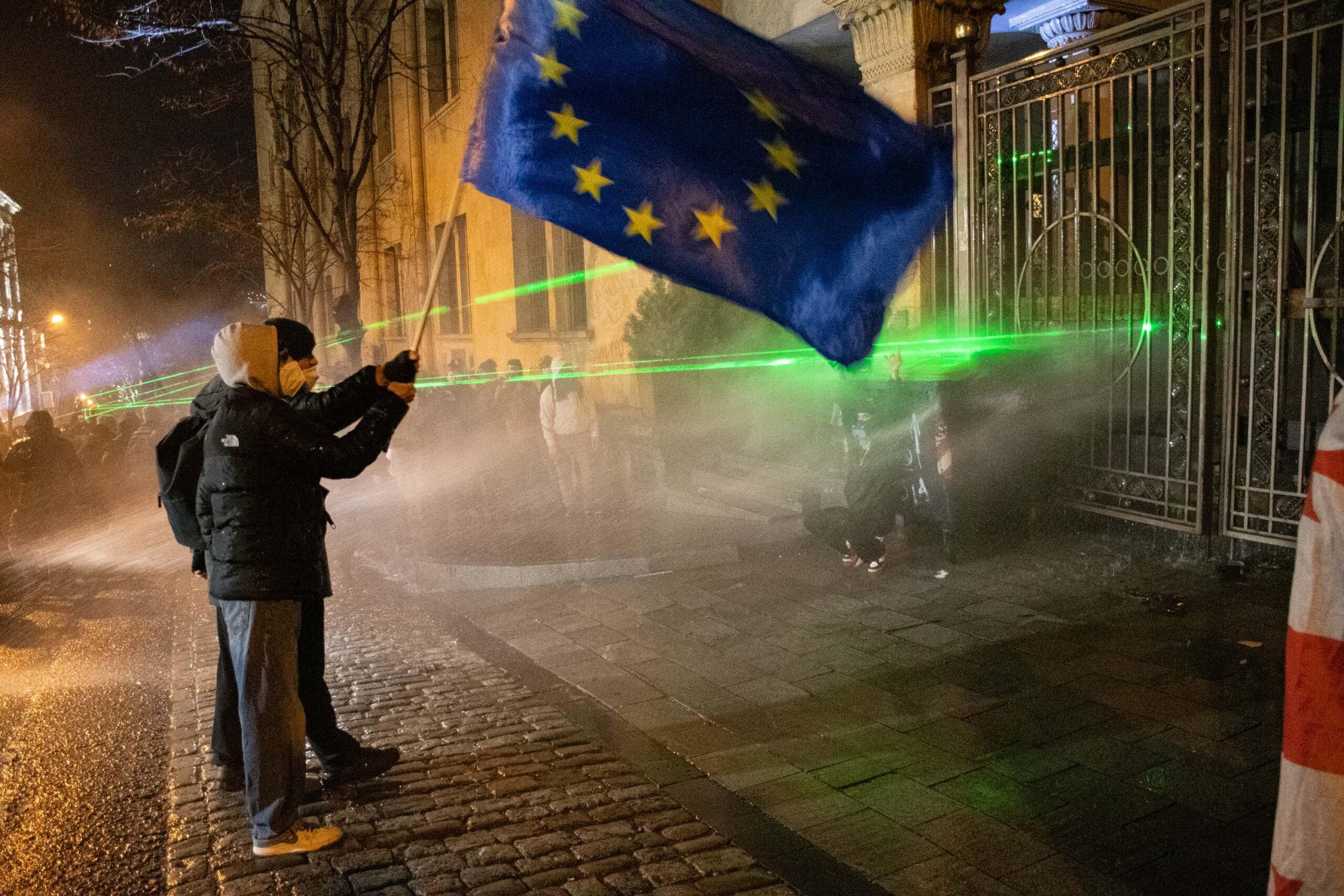 Protesters hold an EU flag in front of the back gates of parliament as riot police use water cannons to disperse the demonstration. Mariam Nikuradze / OC Media.