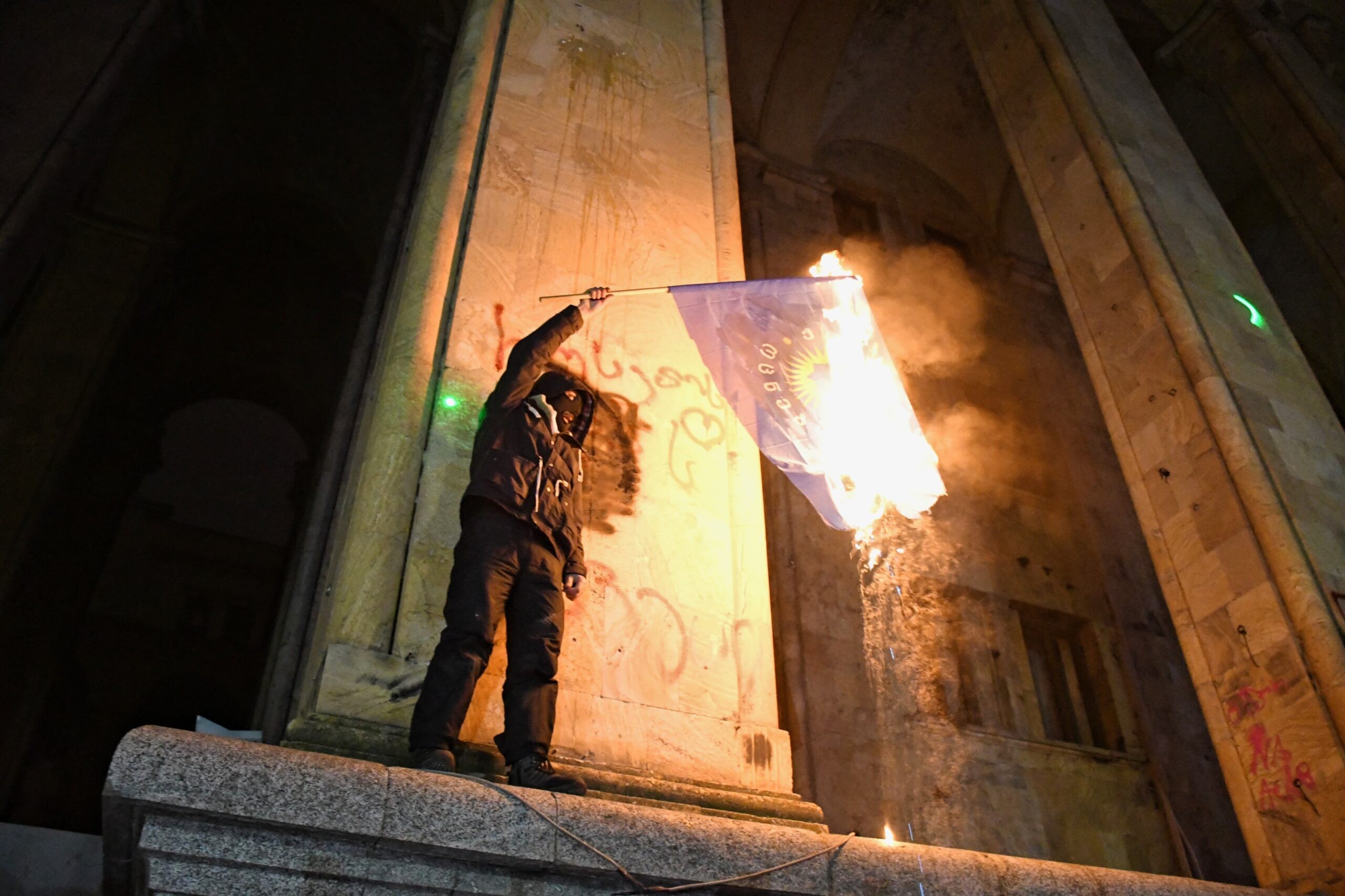 A protester burns the flag of the ruling Georgian Dream party outside the parliament building. Photo: Mariam Nikuradze/OC Media.