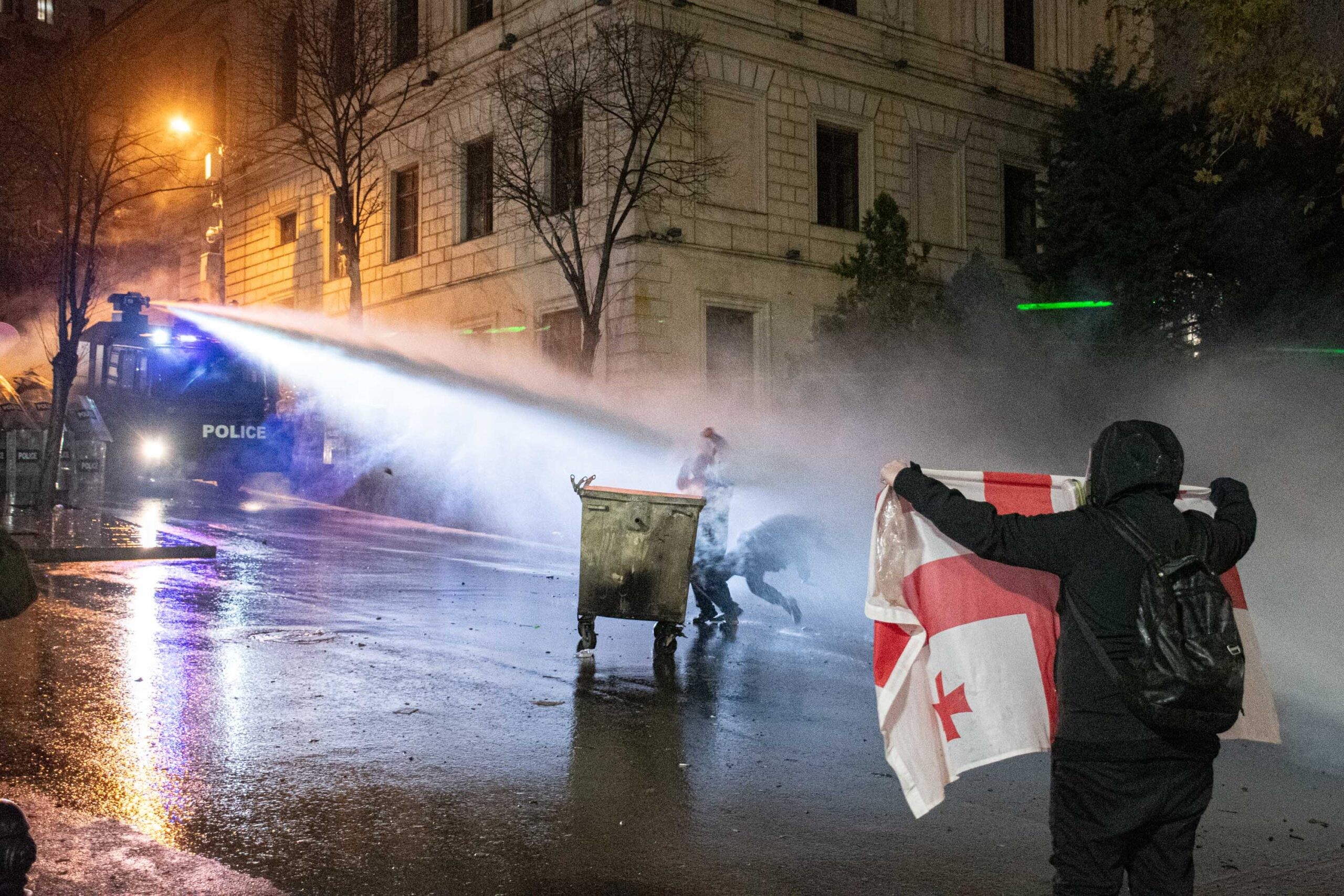 A protester holds a Georgian flag as a water canon is fired at protesters in Tbilisi. Mariam Nikuradze/OC Media.
